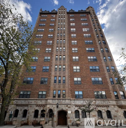 A tall red brick building with many windows and a stone archway at the base.