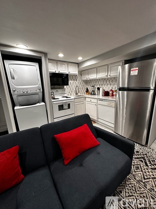 A modern kitchen with a black couch and red pillows.