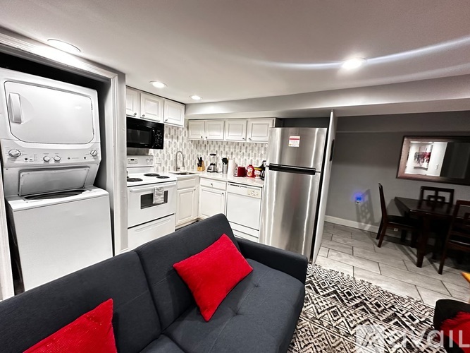 A modern kitchen with a black couch and red pillows.