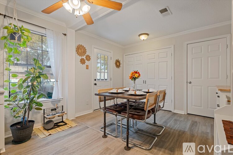 A dining room with a table set for two and a potted plant on the left.