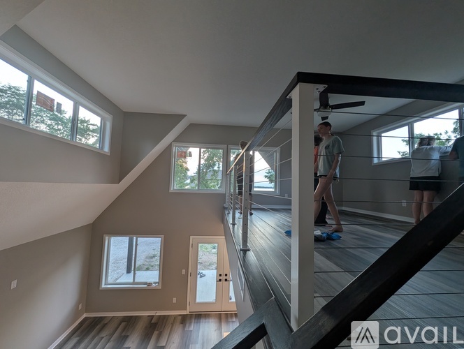 A man is standing in a spacious room with wooden floors and a staircase leading to another level.