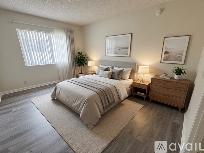 A well-lit bedroom with a large bed, nightstand, and a plant.