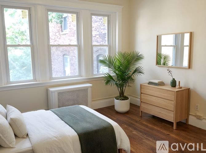 A bedroom with a bed, a plant, and a mirror.