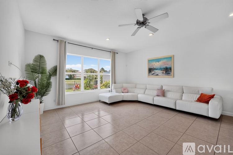 A living room with a white couch, a ceiling fan, and a painting on the wall.