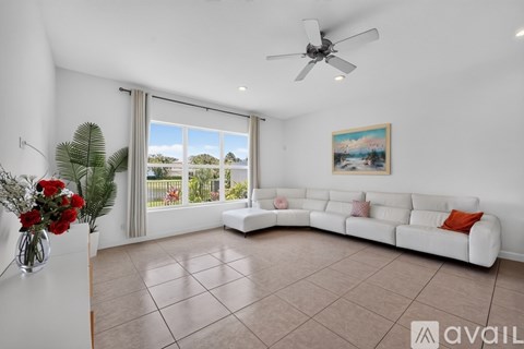 A living room with a white couch, a ceiling fan, and a painting on the wall.