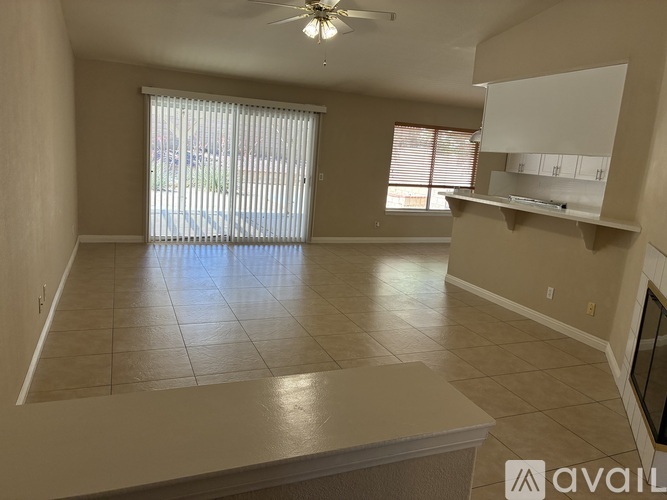 A living room with a fan, tiled floor, and a large window with blinds.