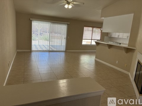 A living room with a fan, tiled floor, and a large window with blinds.