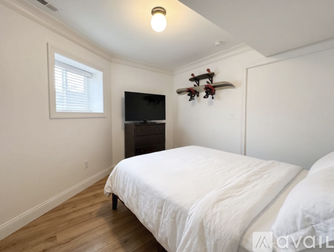 A bedroom with a white bed and a flat screen TV mounted on the wall.