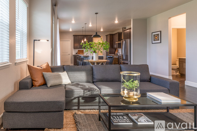 A living room with a grey couch, a glass coffee table, and a plant in a glass vase.