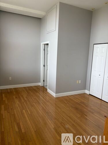 A room with wooden floors and white walls, with a door on the left and a white closet on the right.