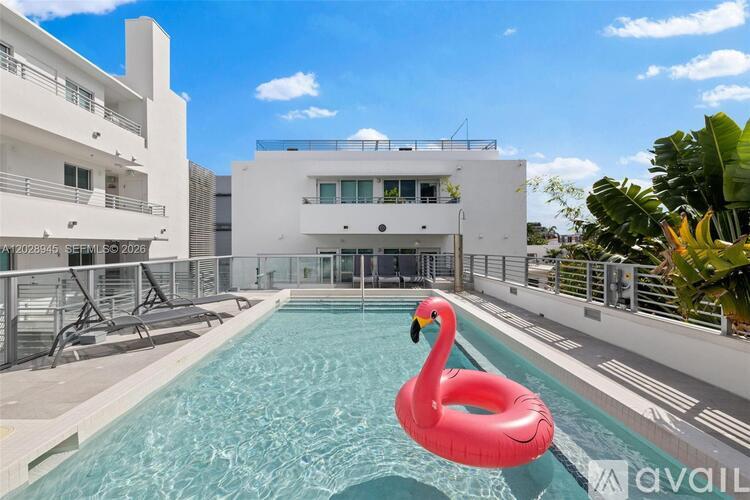 A pink flamingo float sits in a pool in front of a white building.