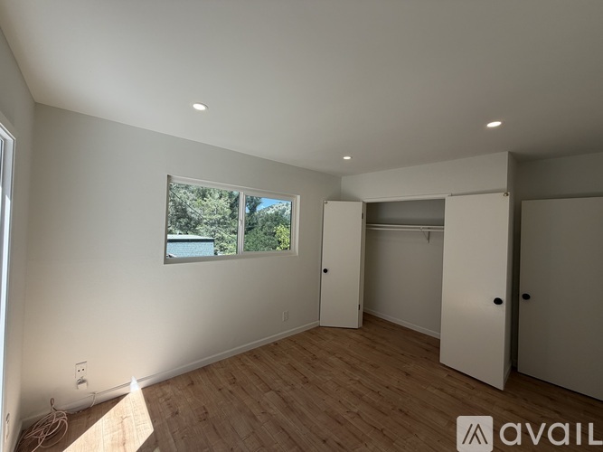 A spacious room with a window, wooden flooring, and white walls.
