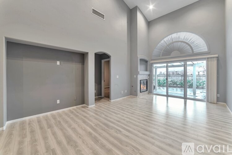 A spacious room with wooden flooring and a large window with a view of a fence.