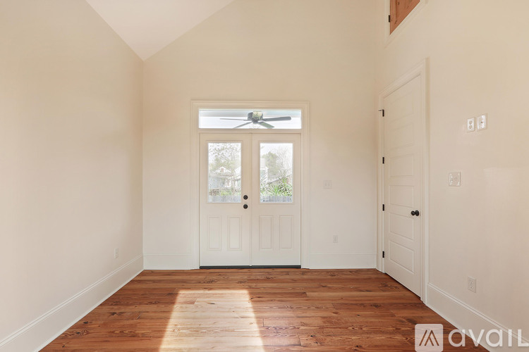 A room with wooden floors and white walls, with a window and a door.