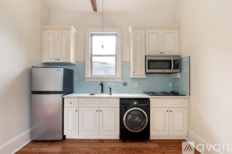 A kitchen with a stainless steel refrigerator, a black washing machine, and white cabinets.