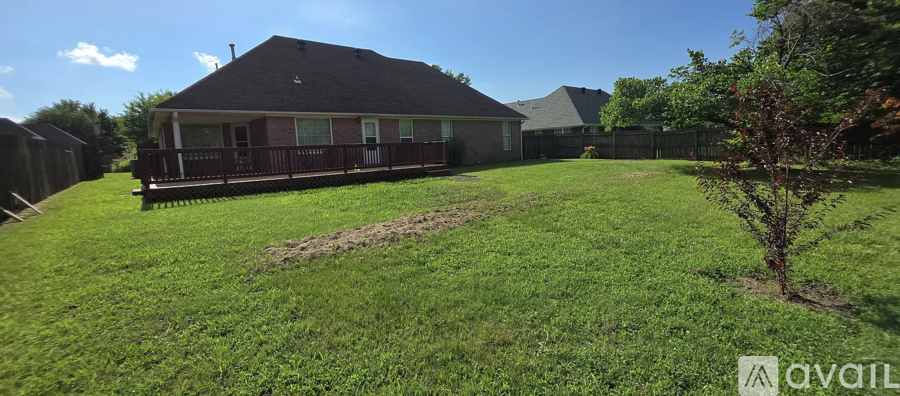 A house with a brown roof and a wooden deck is surrounded by a green lawn.
