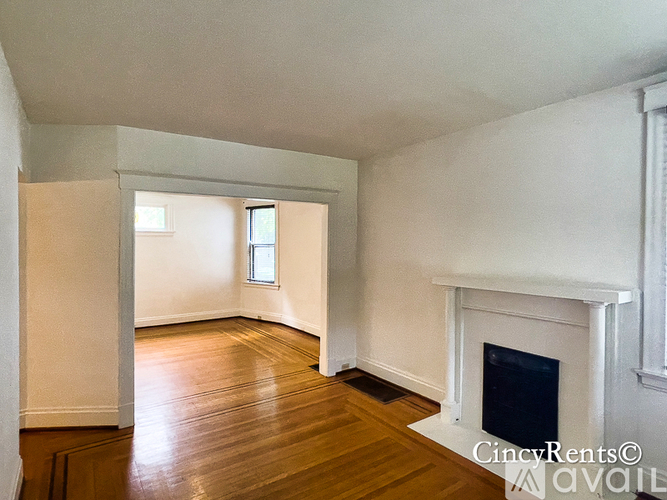 A large empty room with a fireplace and wood flooring.