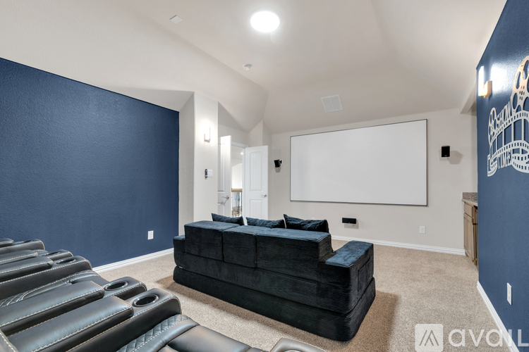 A living room with a black couch and a white screen on the wall.