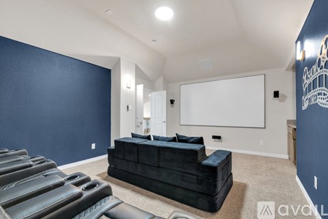 A living room with a black couch and a white screen on the wall.