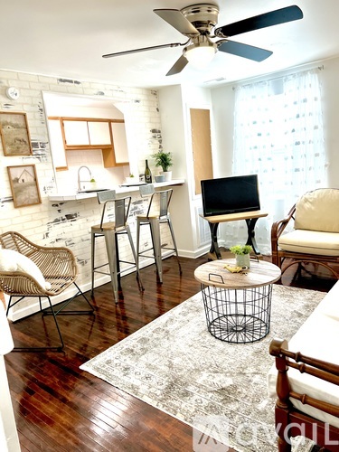 A room with a fan, a table, chairs and a laptop.