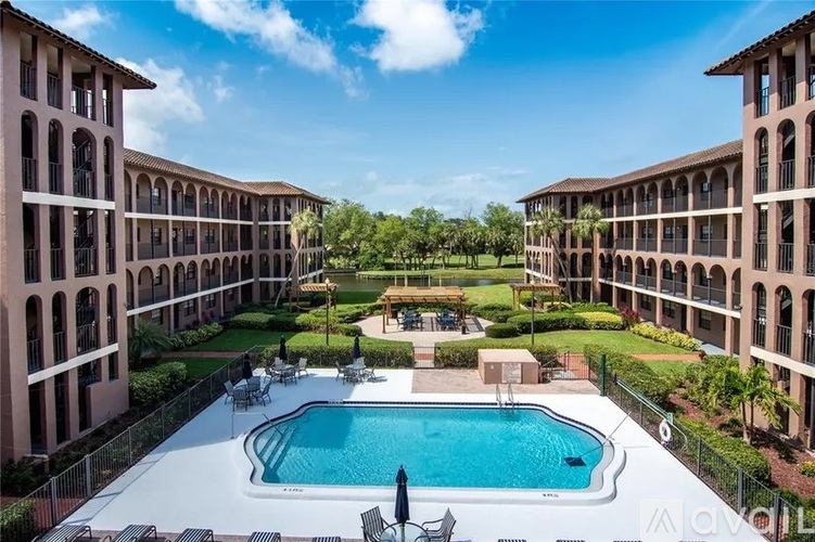 A swimming pool is surrounded by chairs and umbrellas in a courtyard.