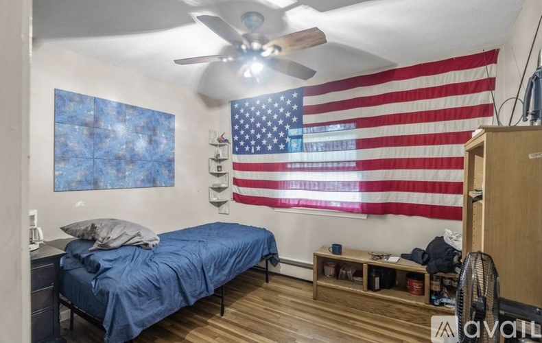 A bedroom with a blue bedspread and an American flag hanging on the wall.