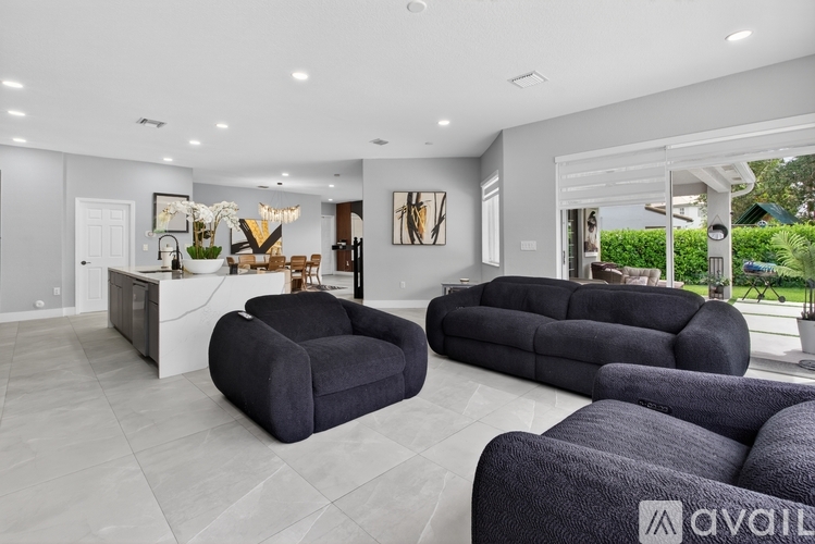 A modern living room with black furniture and a white kitchen area.