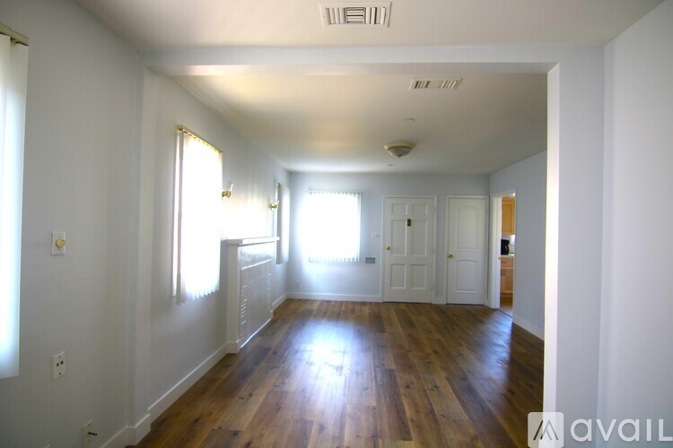 A room with wooden floors and white walls, with sunlight streaming in through the windows.