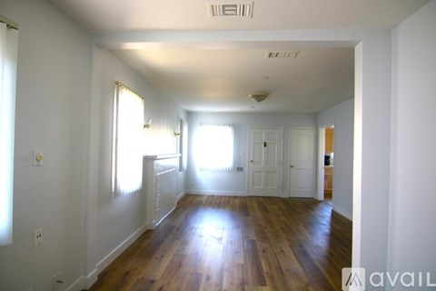 A room with wooden floors and white walls, with sunlight streaming in through the windows.
