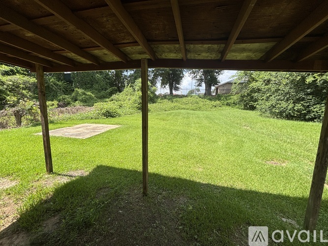 A wooden pergola over a grassy area with a tree and a shed in the background.
