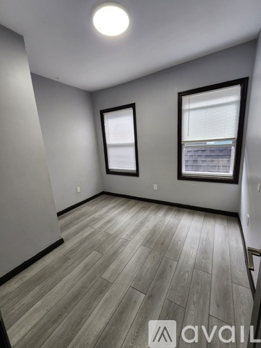 A room with wooden flooring and two windows.