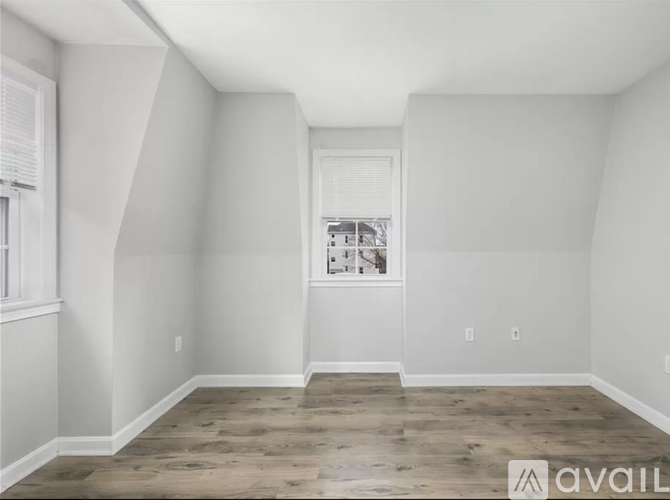 A room with wooden flooring and white walls, with a window showing a view of a house.
