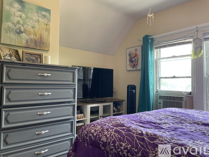 A bedroom with a purple bedspread and a TV on a stand.