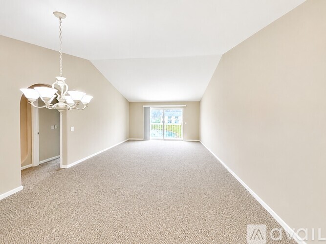 A well-lit, empty room with a chandelier and a carpeted floor.
