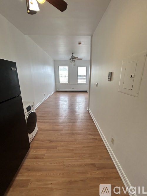 A long hallway with wood floors and a black refrigerator on the left.