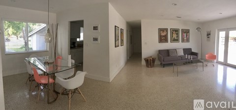 A living room with a glass table and chairs, a grey couch, and a painting on the wall.