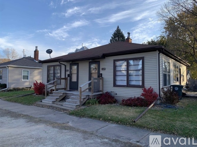 A house with a porch and a front yard with red plants.