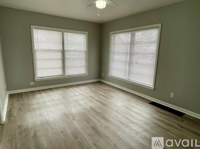 A room with wooden flooring and two windows with blinds.