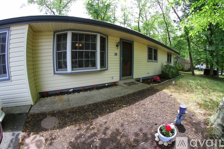 A small yellow house with a window and a door is surrounded by trees.