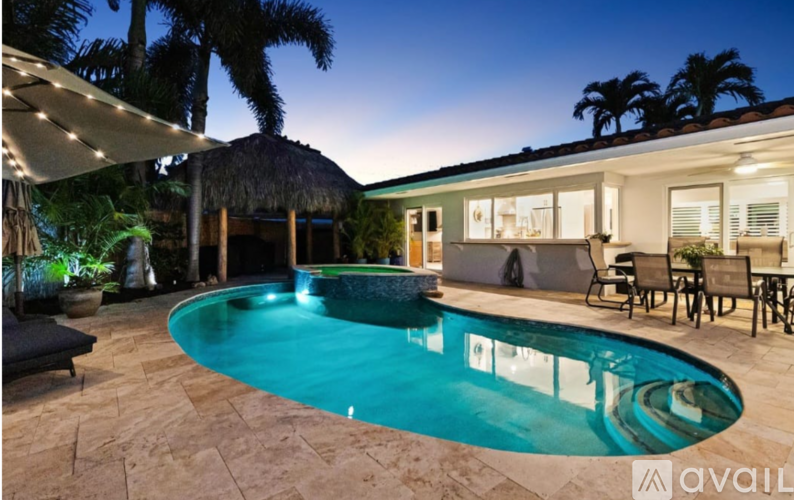A pool in a backyard with a patio and a thatched roof.