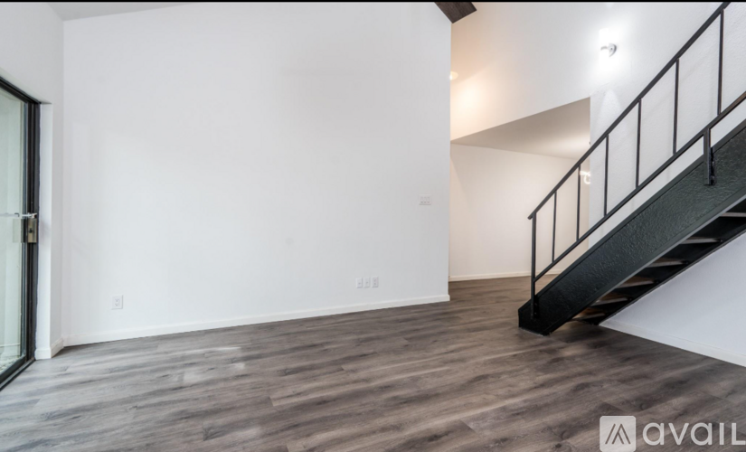 A room with a wooden floor and a staircase with a black railing.