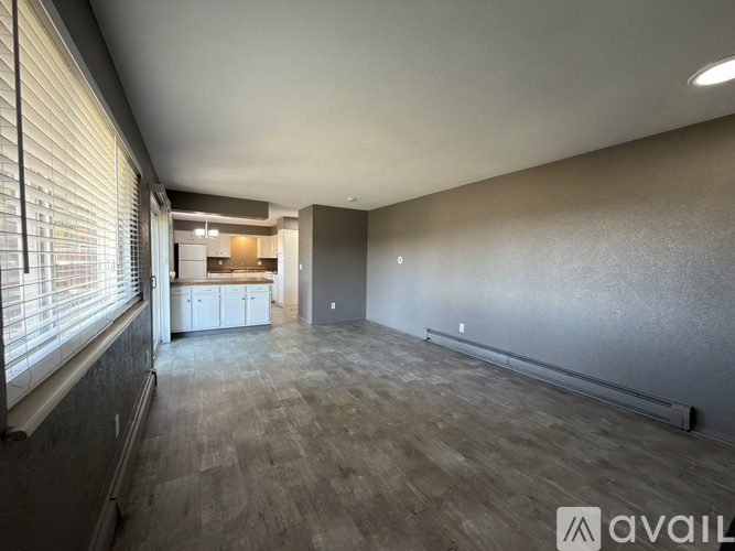 A spacious room with wooden flooring and a window on the left side.