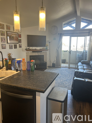 A kitchen with a black counter top and a television above the fireplace.
