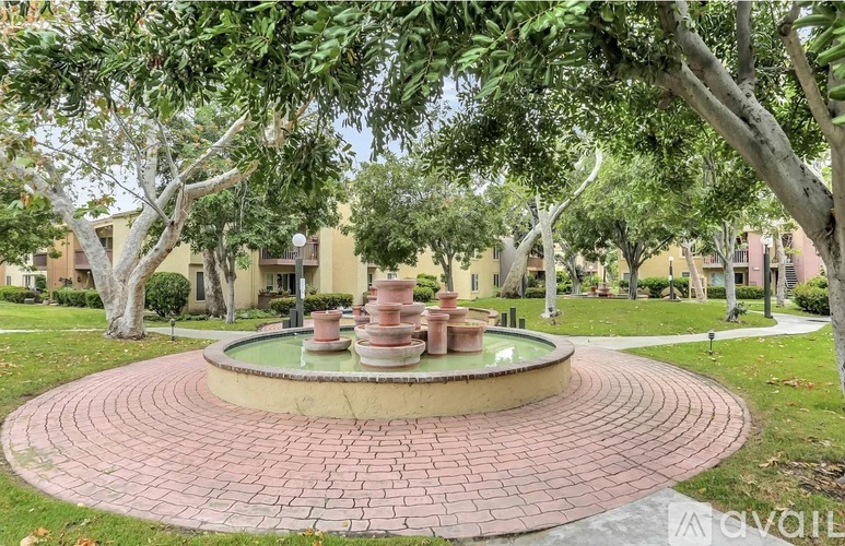 A brick walkway leads to a fountain in a grassy area.