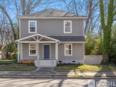 A grey house with a dark blue door and a porch.