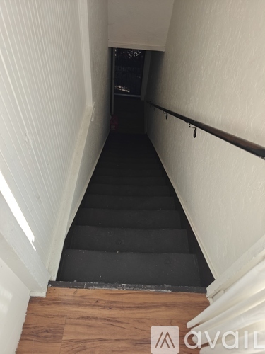 A long, dark staircase with wooden steps and a white wall on the side.
