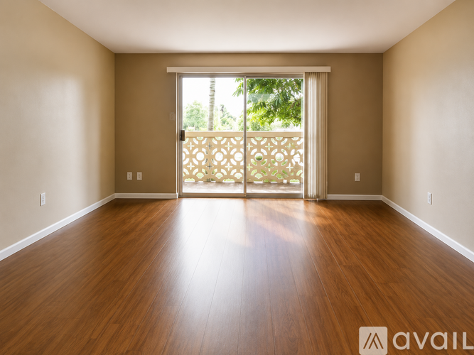 A spacious room with wooden floors and sliding glass doors leading to a balcony.