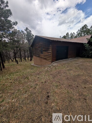 A wooden building with a metal roof is situated in a grassy area with trees in the background.