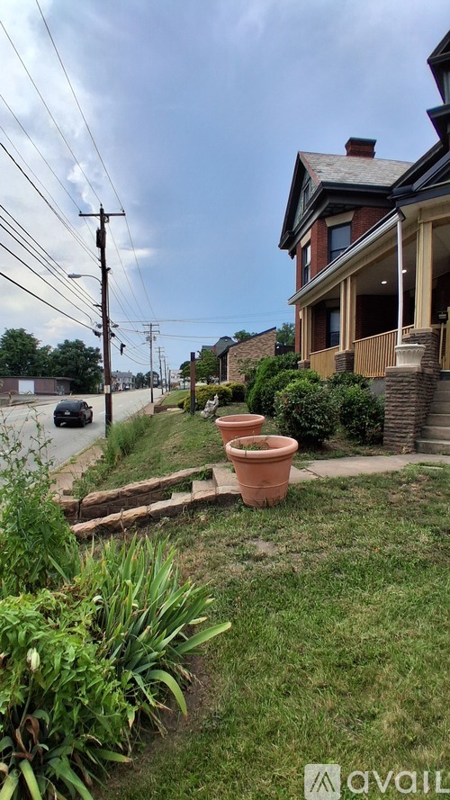 A house with a red brick chimney and a large window is surrounded by a garden with a variety of plants and a small wooden bridge.