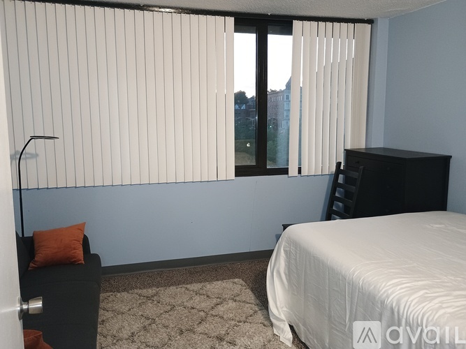 A bedroom with a bed, a chair, and a window with blinds.